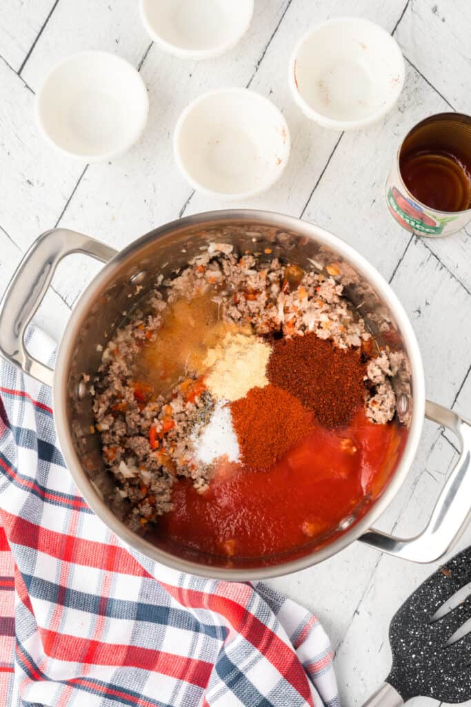 Tomato sauce and seasonings added to ground beef for homemade Texas chili