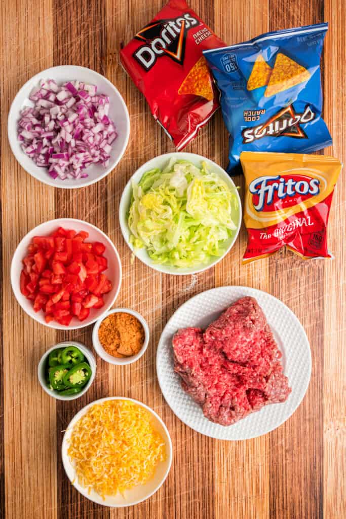 Ingredients for Walking Tacos including ground beef, taco seasoning, corn chips, cheese, lettuce, tomatoes, onions, and jalapeños