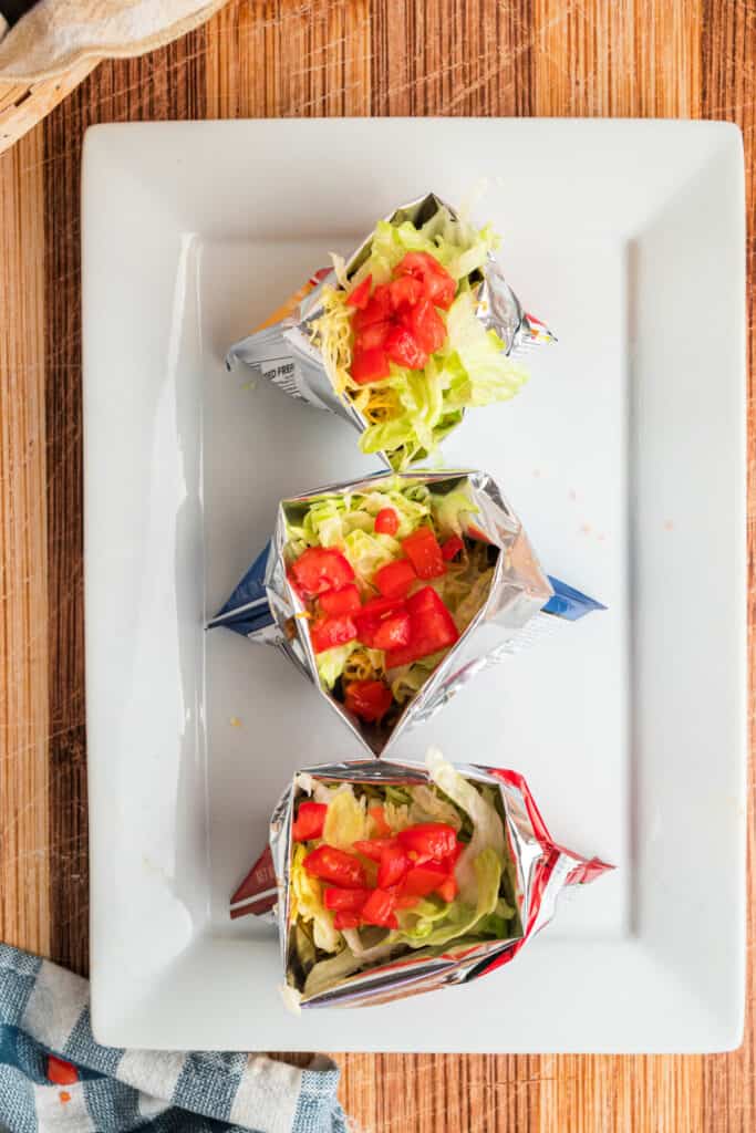 Lettuce and diced tomatoes added to Walking Tacos in individual chip bags