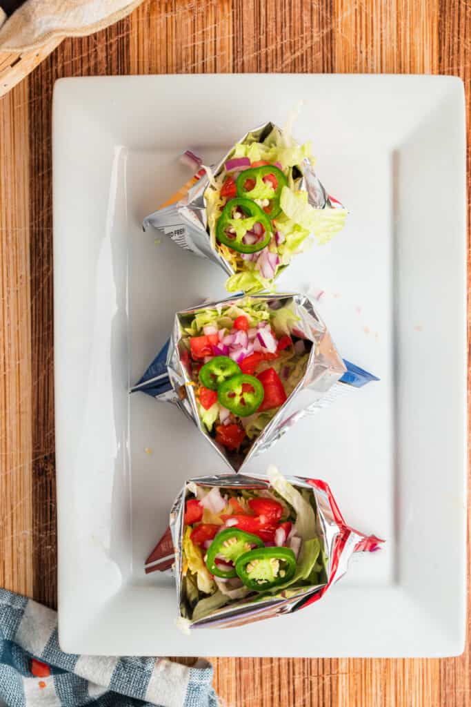 Walking Tacos topped with lettuce, tomatoes, red onion, and sliced jalapeños