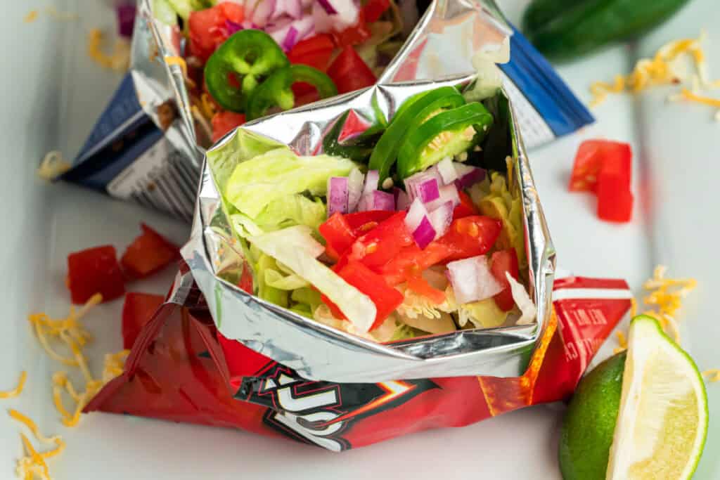 Close-up of a Walking Taco served in a chip bag with lettuce, tomatoes, onions, and sliced jalapeños
