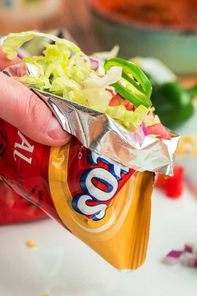 Walking Taco held in a corn chip bag and topped with lettuce, tomatoes, onions, and fresh jalapeños