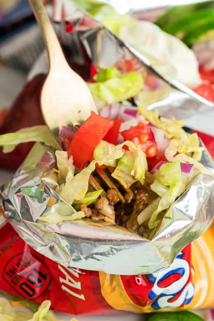 Forkful of seasoned ground beef, lettuce, tomatoes, and onions from a Walking Taco