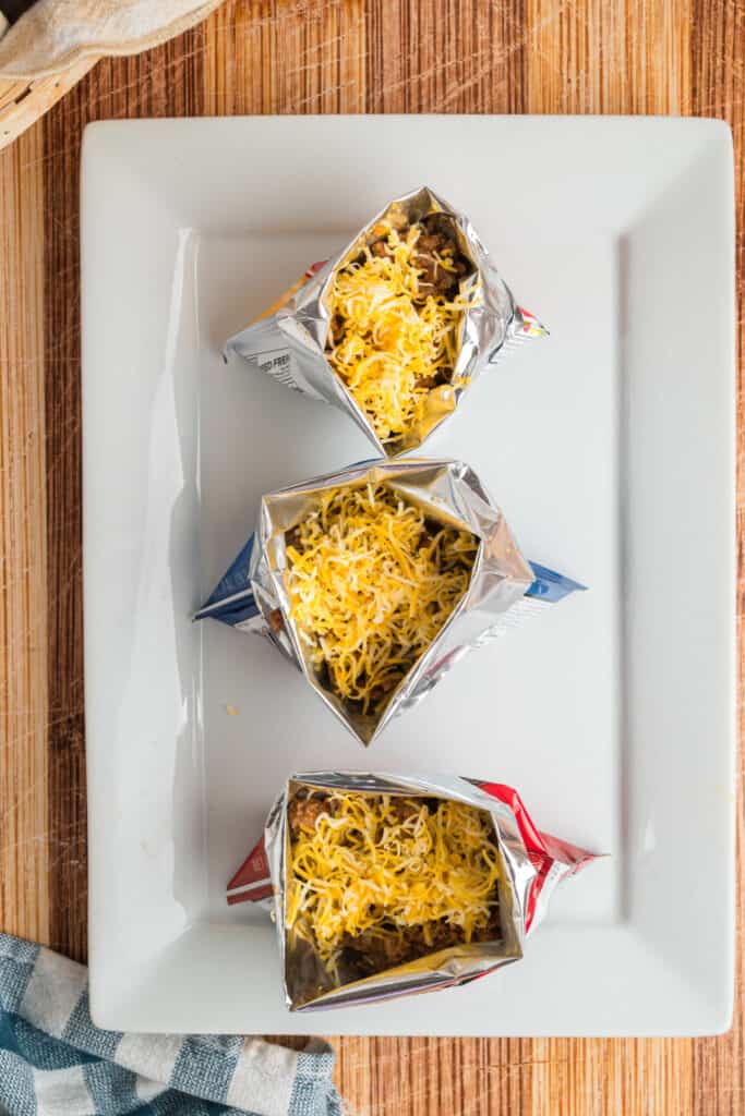 Shredded cheese added over warm taco meat in individual chip bags