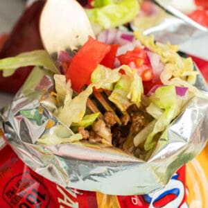 Walking Tacos with seasoned ground beef, cheese, lettuce, tomatoes, onions, and jalapeños served in a corn chip bag