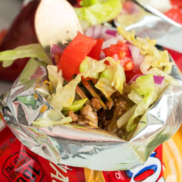 Walking Tacos with seasoned ground beef, cheese, lettuce, tomatoes, onions, and jalapeños served in a corn chip bag