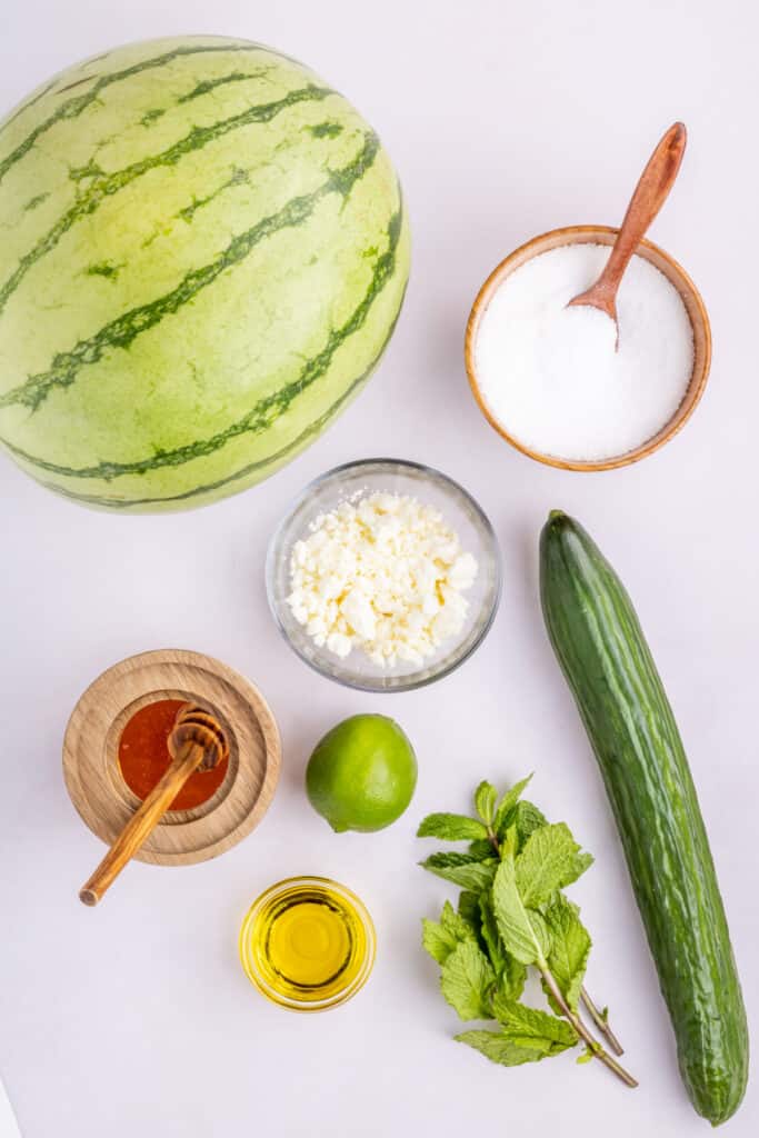 Ingredients for Watermelon Feta Mint Salad including watermelon, English cucumber, feta cheese, fresh mint, honey, lime, olive oil, and salt.
