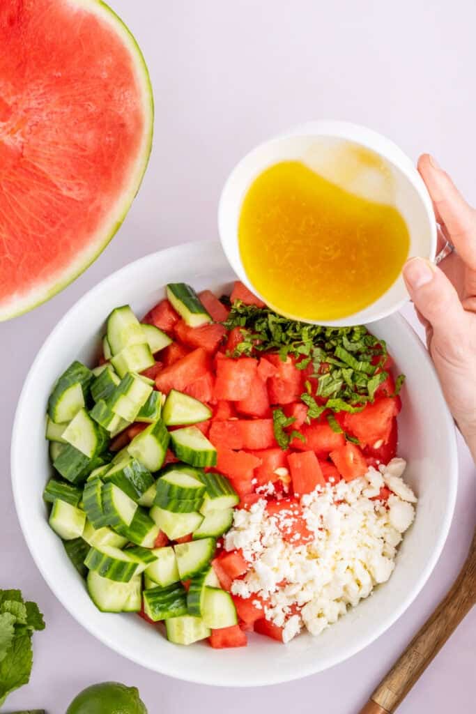 Honey lime dressing being poured over Watermelon Feta Mint Salad before tossing.