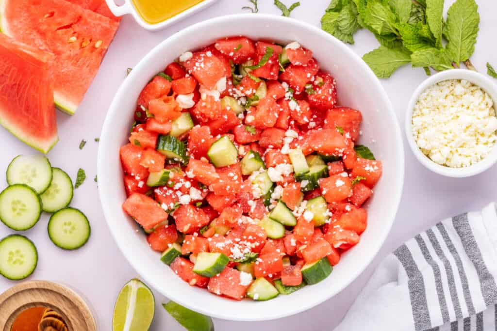 Watermelon Feta Mint Salad served in a white bowl with fresh mint, feta cheese, cucumber, and watermelon wedges.