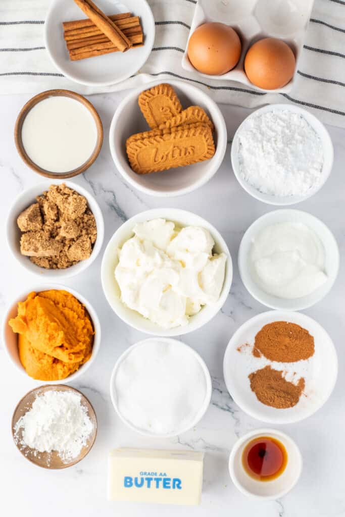 Ingredients for mini pumpkin cheesecakes arranged in bowls, including pumpkin puree, cream cheese, Biscoff cookies, eggs, sugar, and spices.
