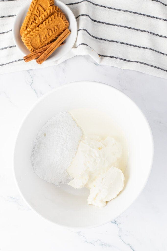 Cream cheese, powdered sugar, and heavy cream in a bowl for making the cheesecake glaze.