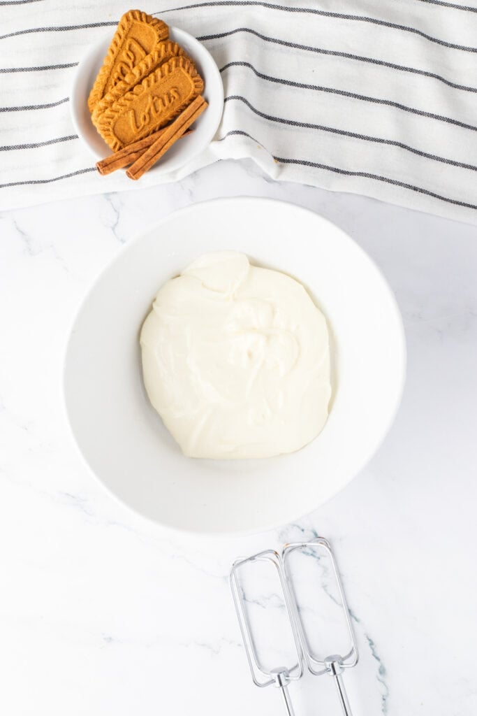 Smooth cream cheese glaze in a mixing bowl with electric mixer beaters beside it.