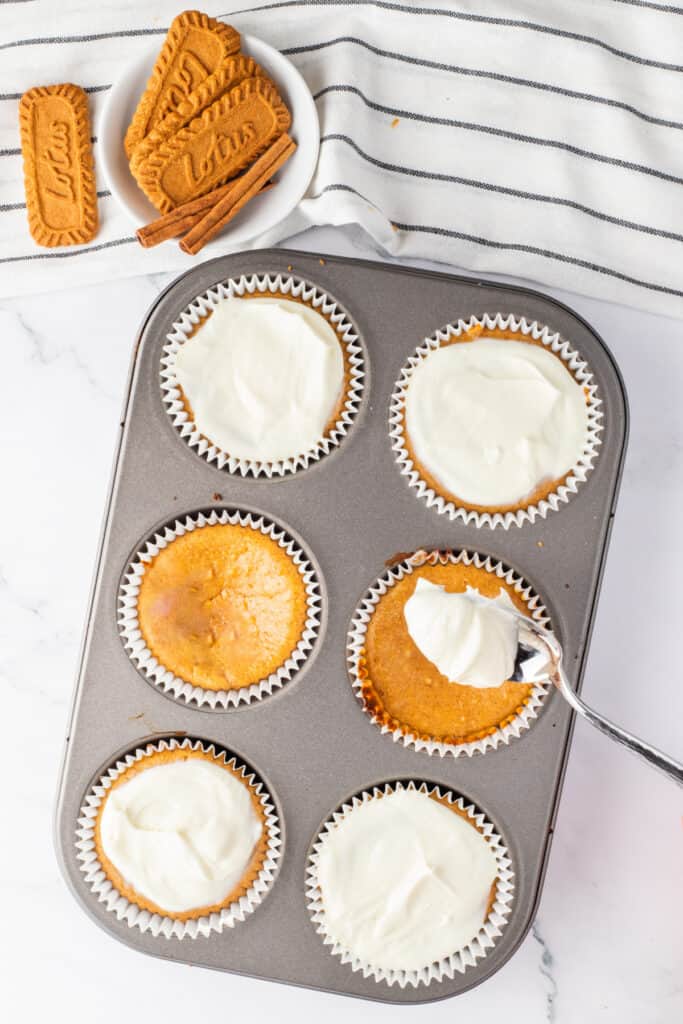 Cream cheese glaze being spooned over baked mini pumpkin cheesecakes in a muffin pan.