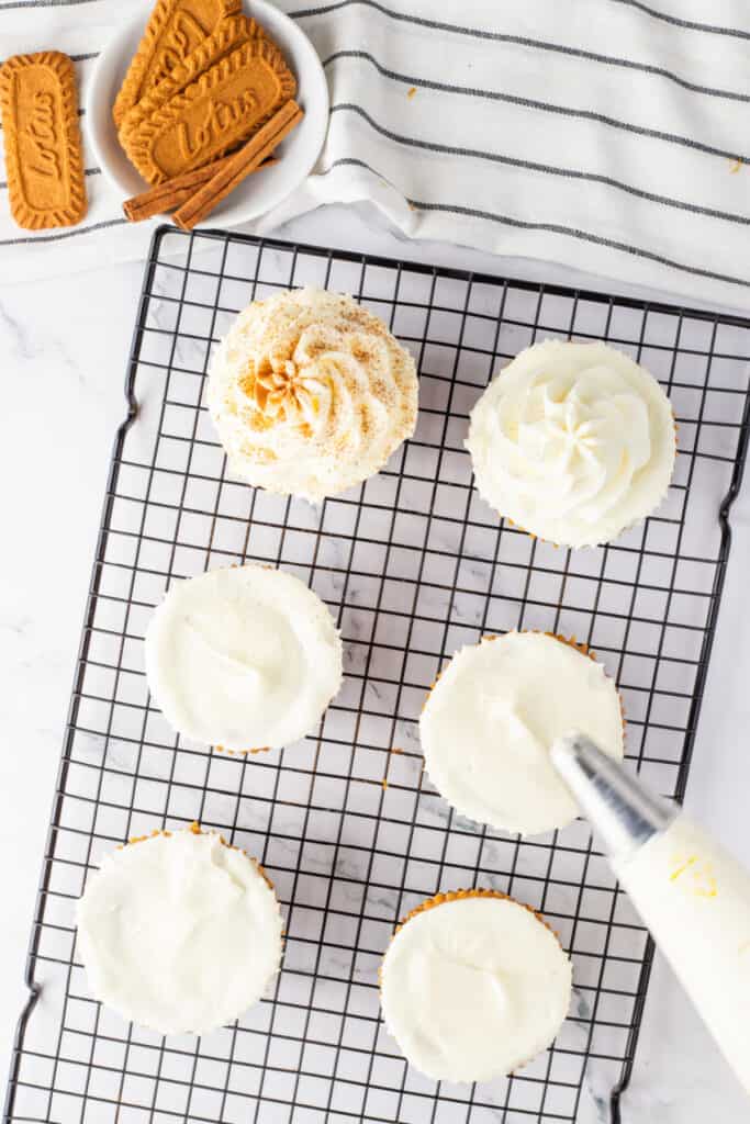 Mini pumpkin cheesecakes on a cooling rack being decorated with whipped cream.