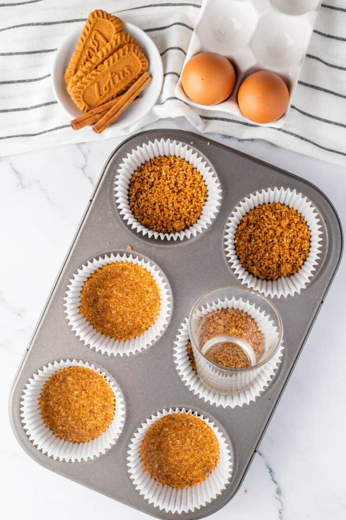 Biscoff cookie crusts pressed firmly into lined muffin cups before baking.