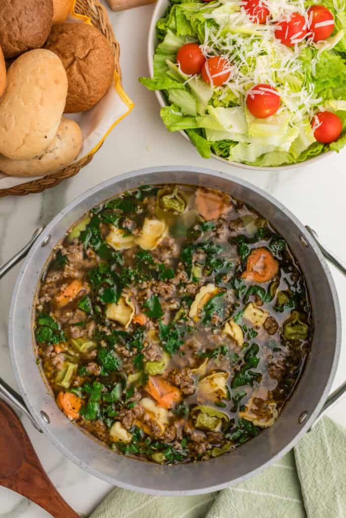 One-Pot Sausage Tortellini Soup in a stockpot served alongside bread and a fresh green salad.
