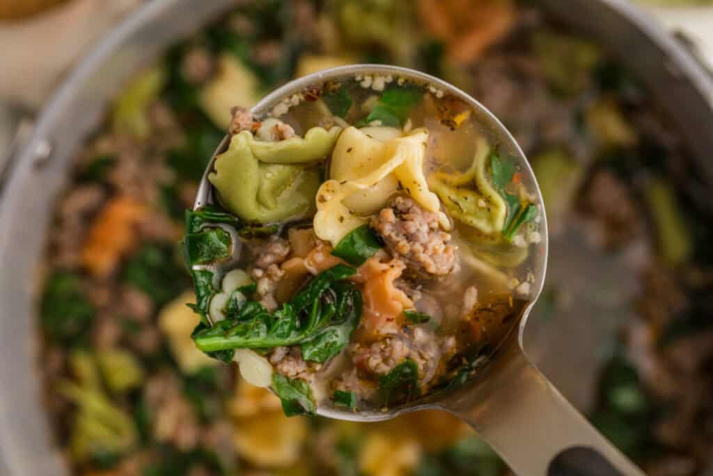 Ladle filled with sausage tortellini soup showing tender tortellini, Italian sausage, spinach, and seasoned broth.