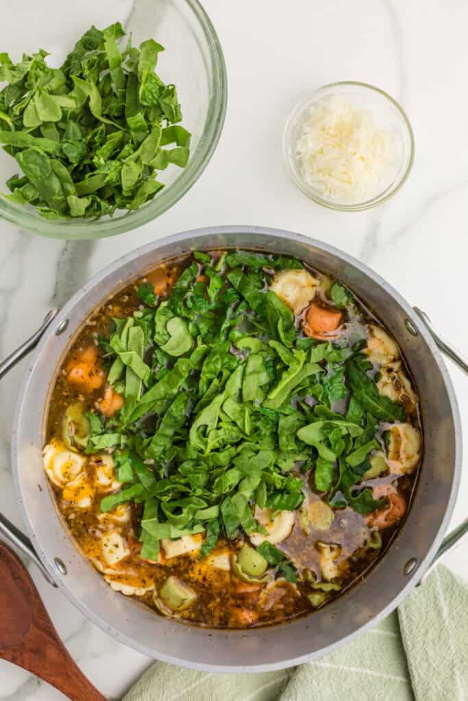 Fresh chopped baby spinach added to tortellini and Italian sausage soup in a large stockpot.