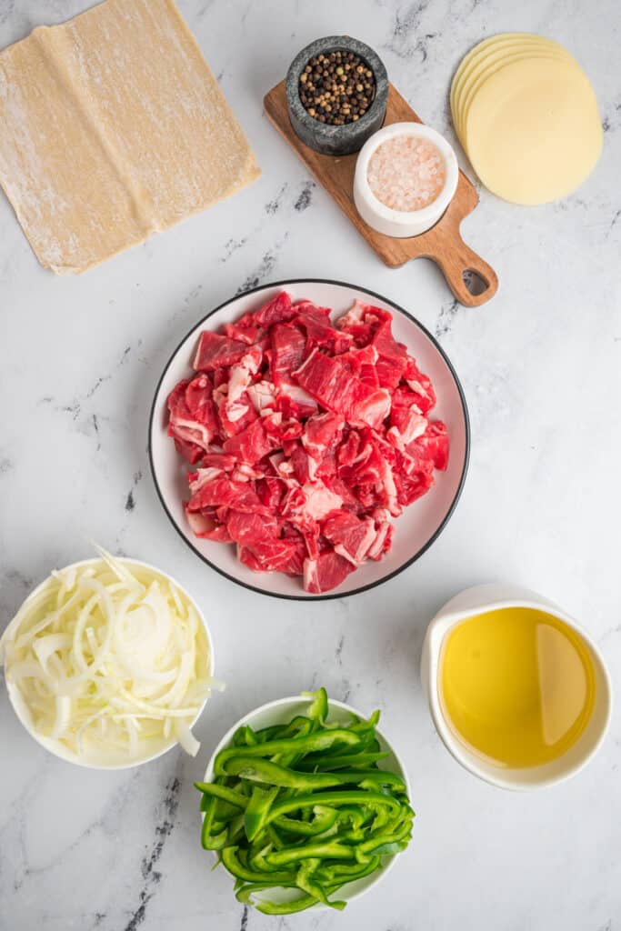 Ingredients for Philly Cheesesteak Egg Rolls including sliced steak, green bell pepper, onion, provolone, and egg roll wrappers