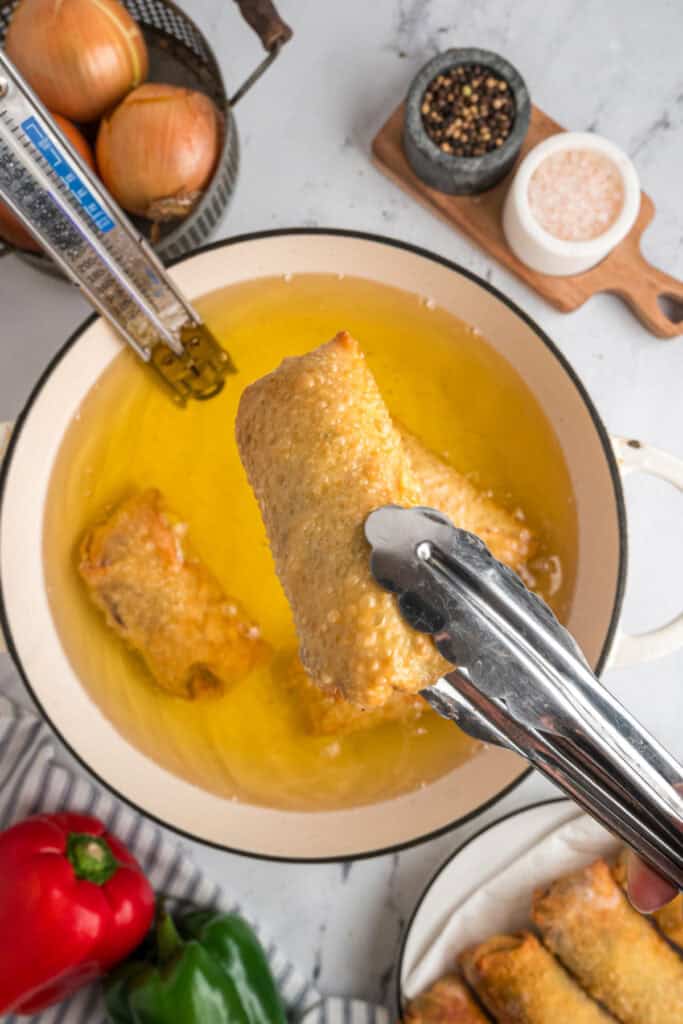 Golden brown Philly Cheesesteak Egg Roll being removed from the hot frying oil with tongs