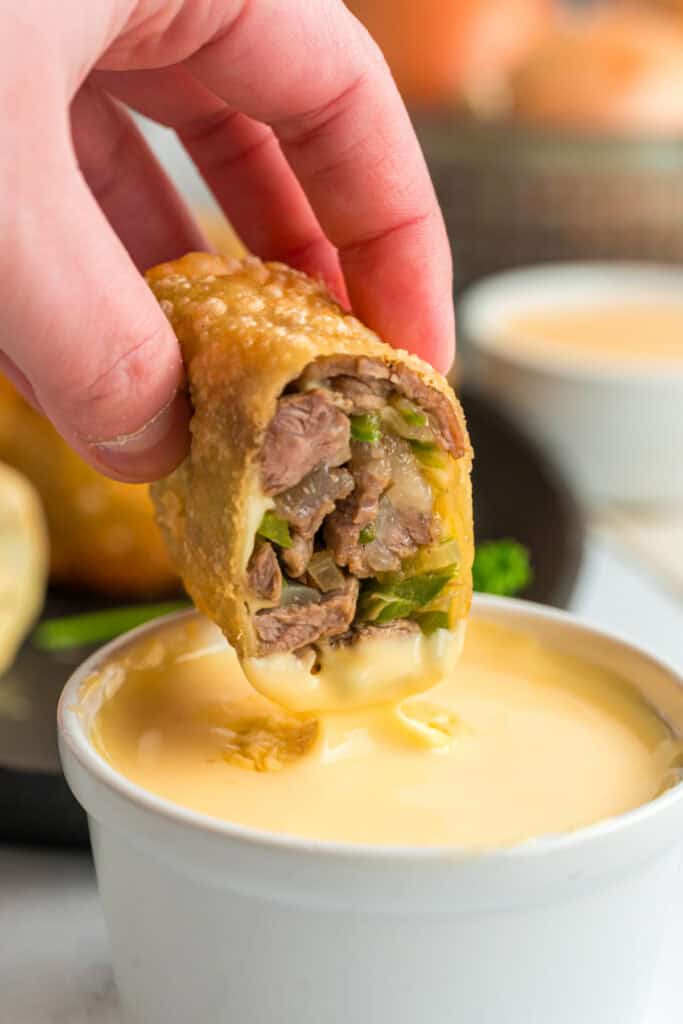 Crispy Philly Cheesesteak Egg Roll filled with steak, peppers, onions, and provolone dipped in cheese sauce