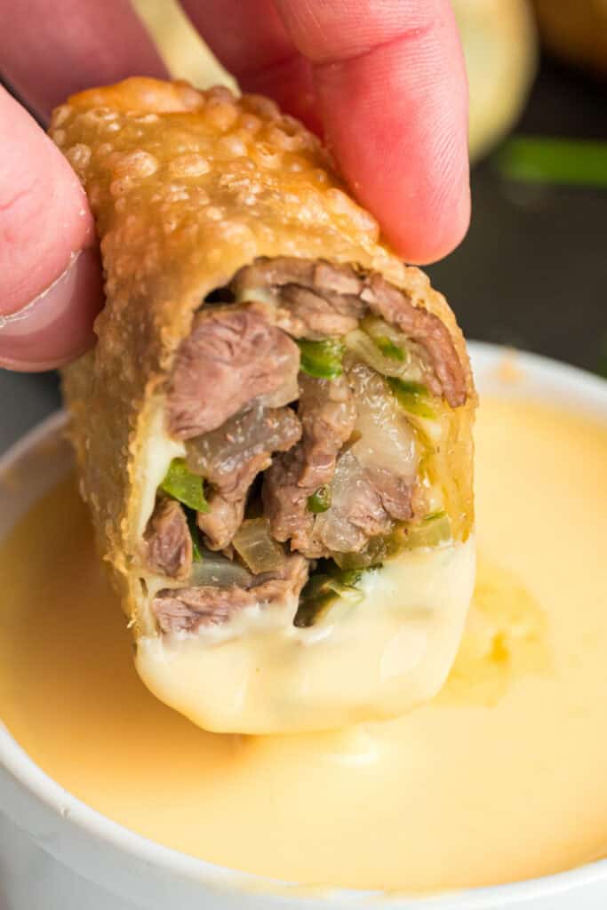 Crispy steak and cheese egg roll dipped into creamy cheese sauce