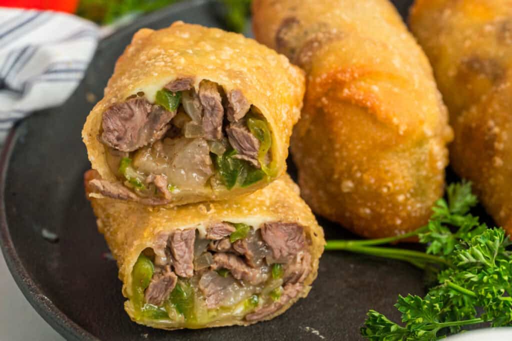 Sliced Philly Cheesesteak Egg Rolls filled with steak, peppers, onions, and melted provolone on a serving plate