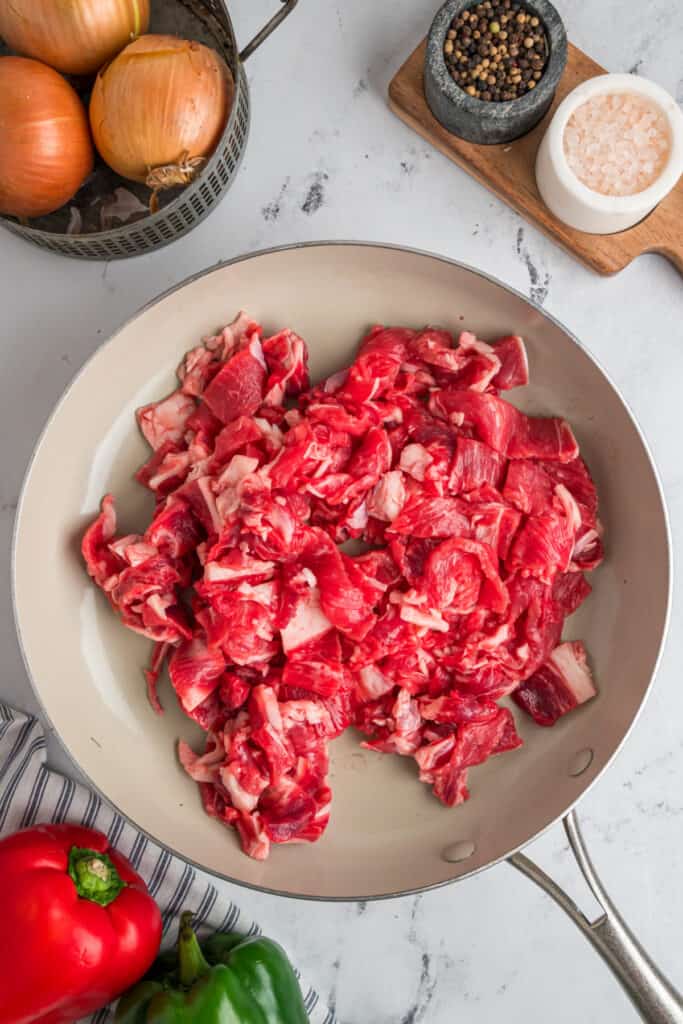 Thinly sliced steak cooking in a large skillet for Philly Cheesesteak Egg Rolls