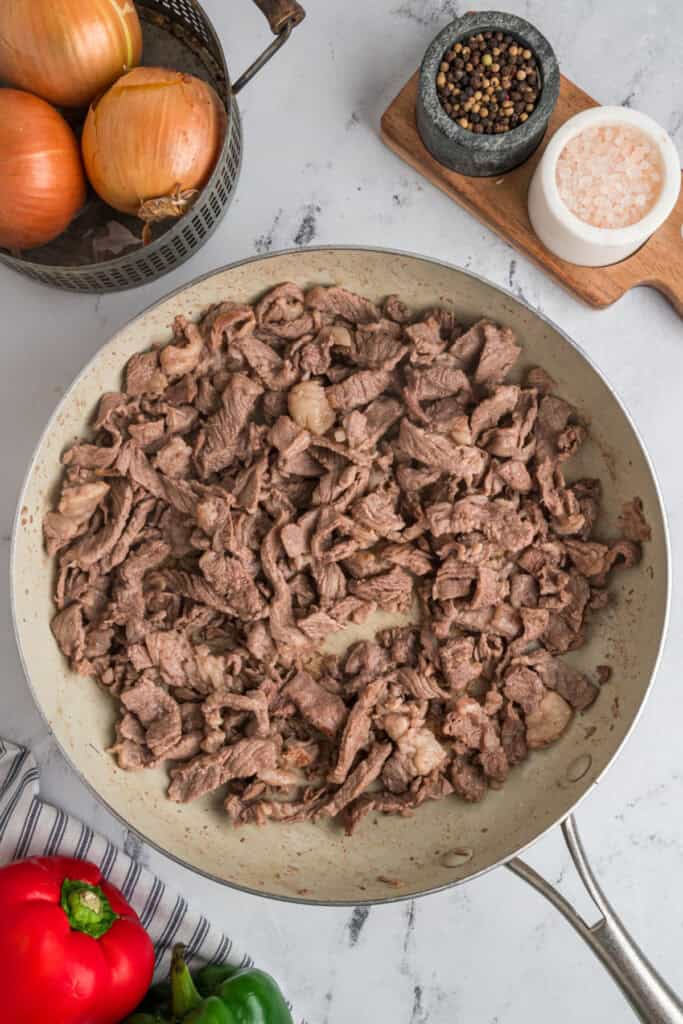 Browned thinly sliced steak in a skillet seasoned with salt and black pepper