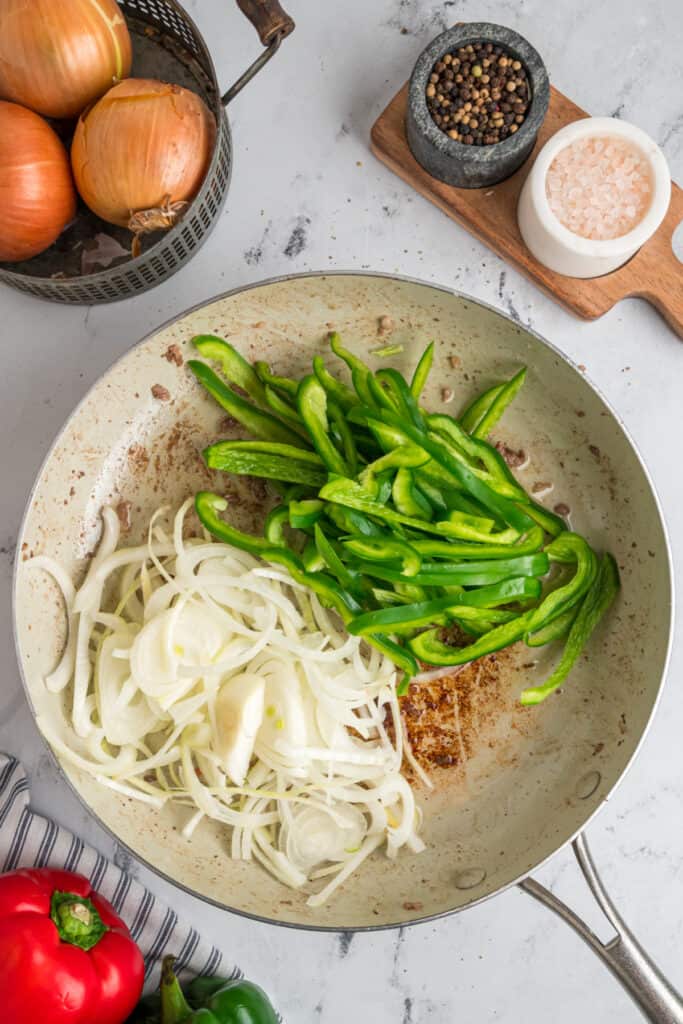 Thinly sliced green bell pepper and onion added to a skillet for the cheesesteak filling
