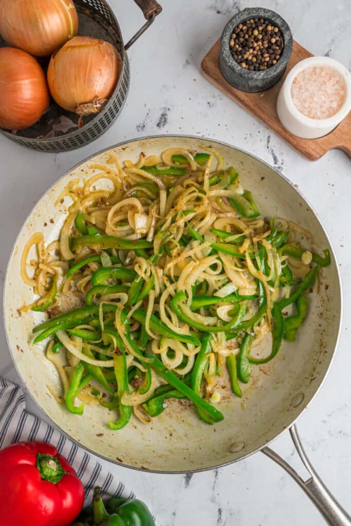 Sautéed green bell peppers and onions cooking until tender and lightly caramelized