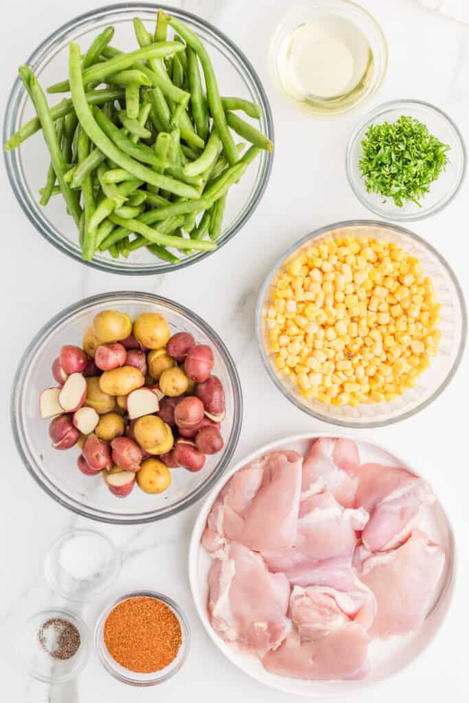 Ingredients for Sheet Pan Blackened Chicken Thighs, including chicken thighs, baby potatoes, green beans, corn, blackened seasoning, olive oil, and parsley.