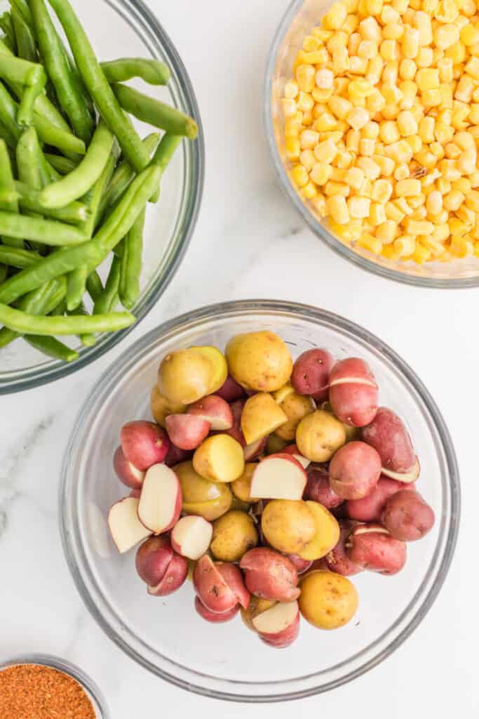 Halved baby potatoes in a mixing bowl with fresh green beans and frozen sweet corn nearby.