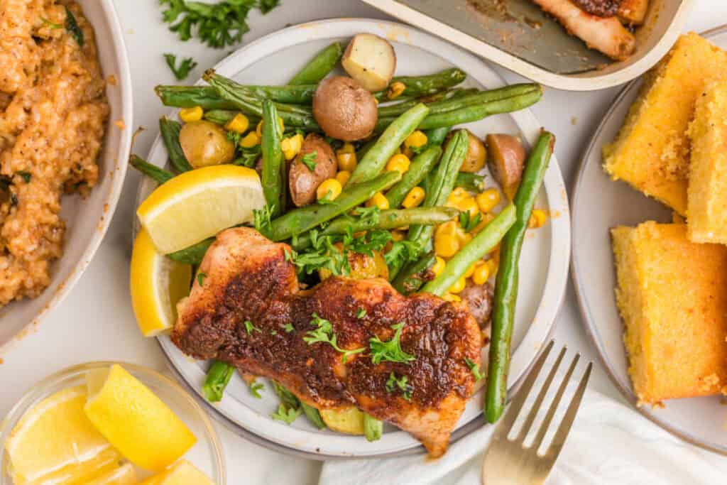 Blackened chicken thighs served with roasted baby potatoes, green beans, corn, lemon, cornbread, and rice.