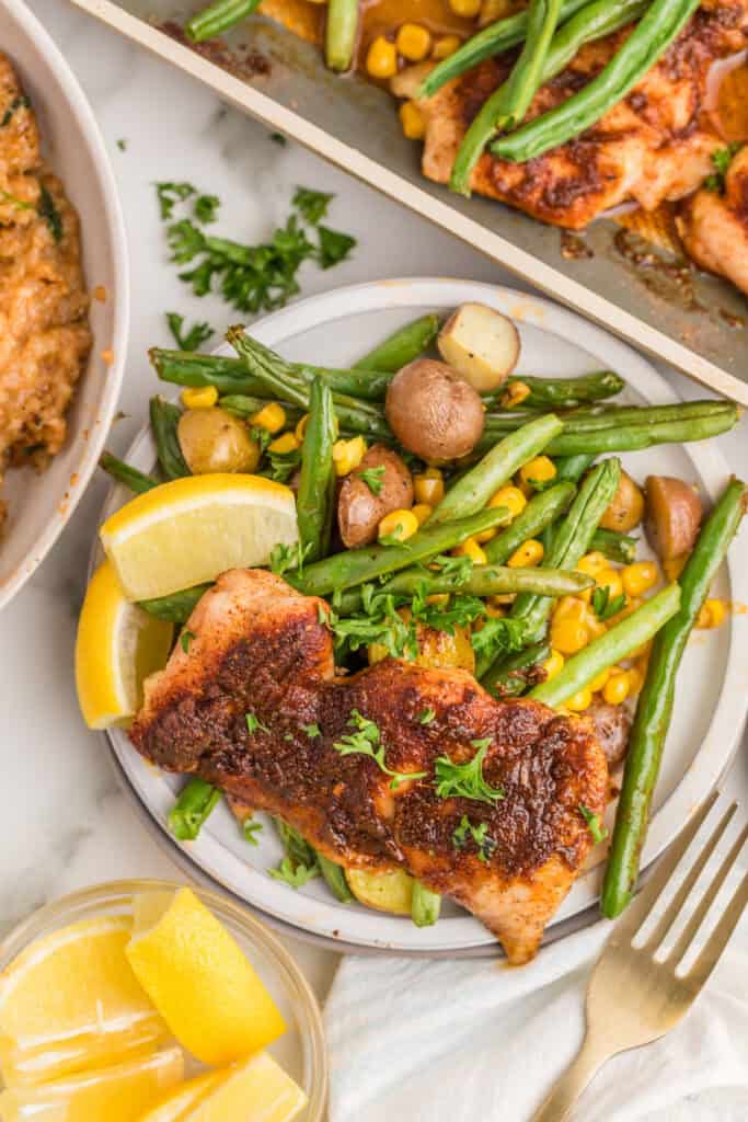 Sheet Pan Blackened Chicken Thighs served with roasted baby potatoes, green beans, corn, and fresh lemon.