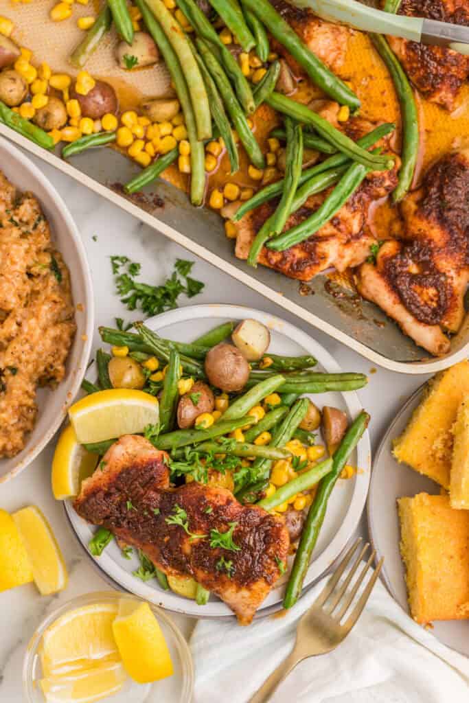 Blackened chicken thighs with roasted baby potatoes, green beans, and corn served alongside cornbread and rice.