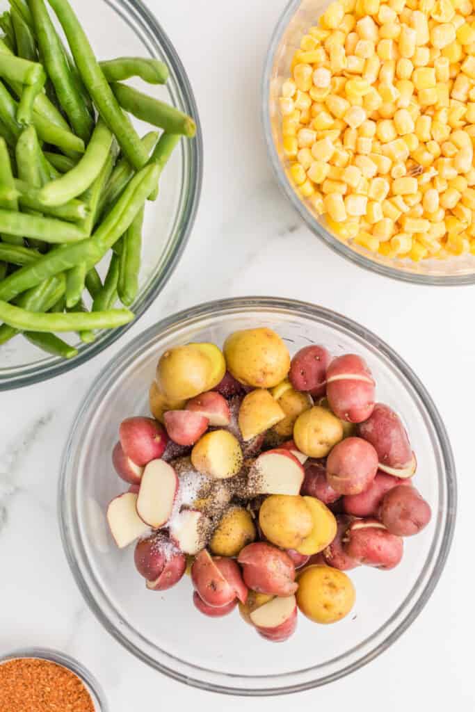Baby potatoes seasoned with salt and black pepper in a glass mixing bowl.