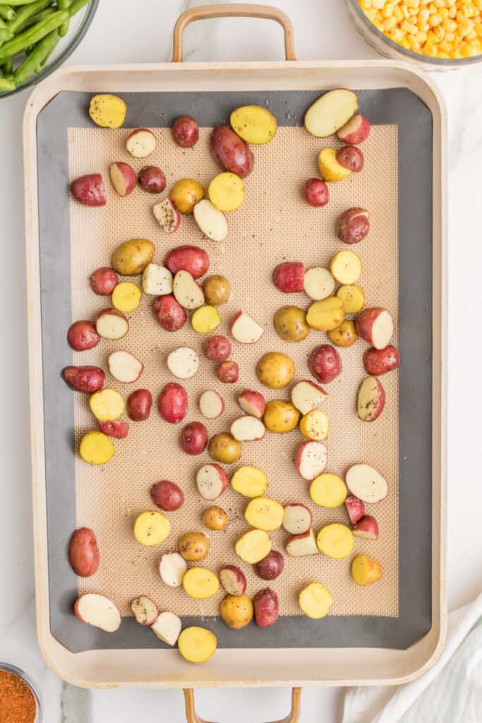 Seasoned baby potatoes spread on a lined sheet pan before roasting.