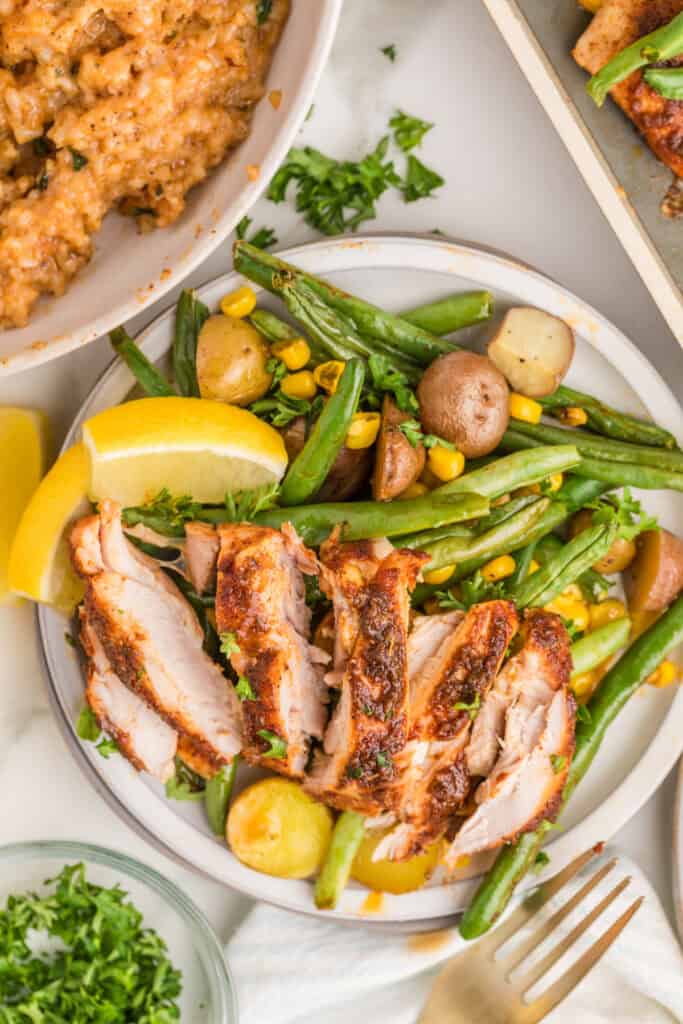 Sliced blackened chicken thighs served with roasted green beans, baby potatoes, sweet corn, and lemon.