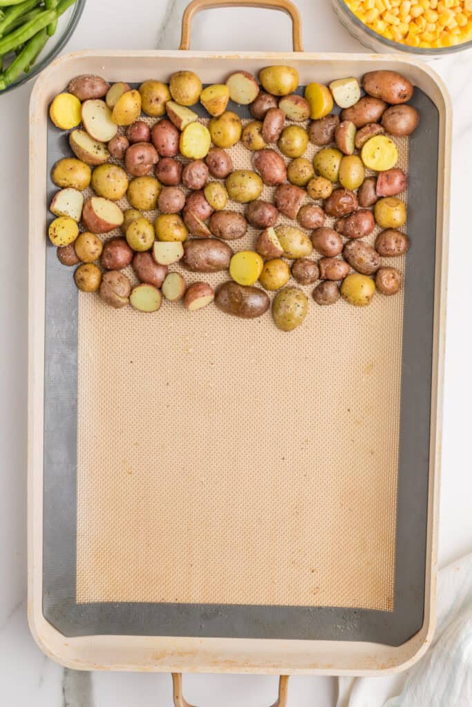 Partially roasted baby potatoes moved to one side of a sheet pan to make room for the chicken.