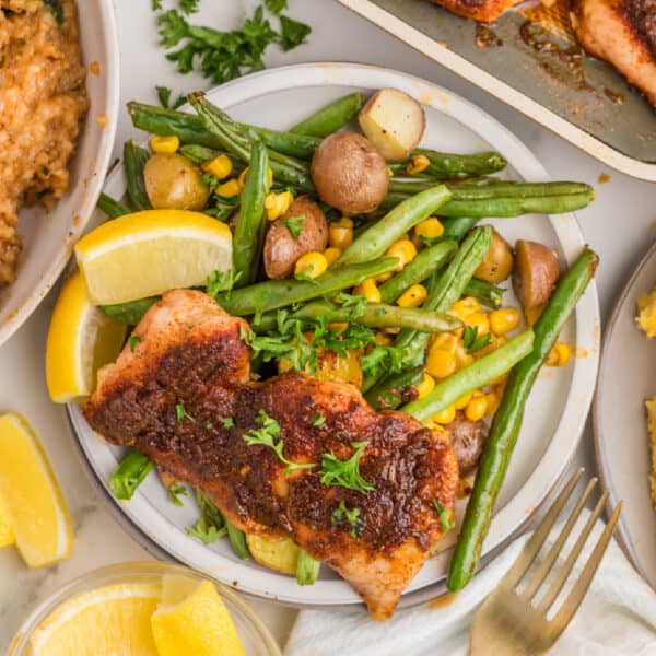 Blackened chicken thighs served over roasted baby potatoes, green beans, corn, parsley, and lemon wedges.