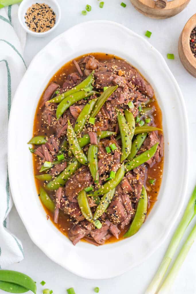 Slow Cooker Asian Pot Roast with shredded beef, snap peas, green onions, sesame seeds, and soy-ginger sauce