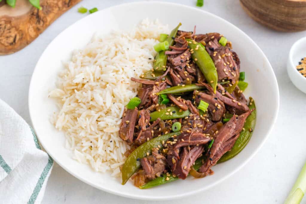 Asian pot roast served with white rice, snap peas, green onions, and sesame seeds
