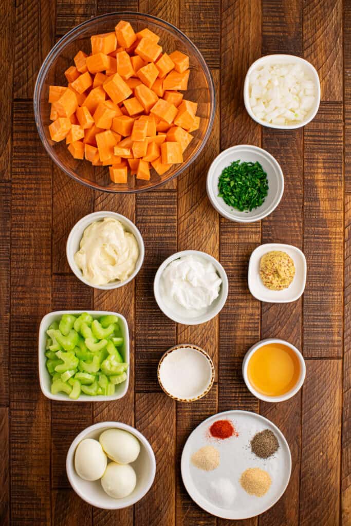 Ingredients for homemade Sweet Potato Salad arranged in bowls, including cubed sweet potatoes, eggs, celery, onion, and creamy dressing ingredients