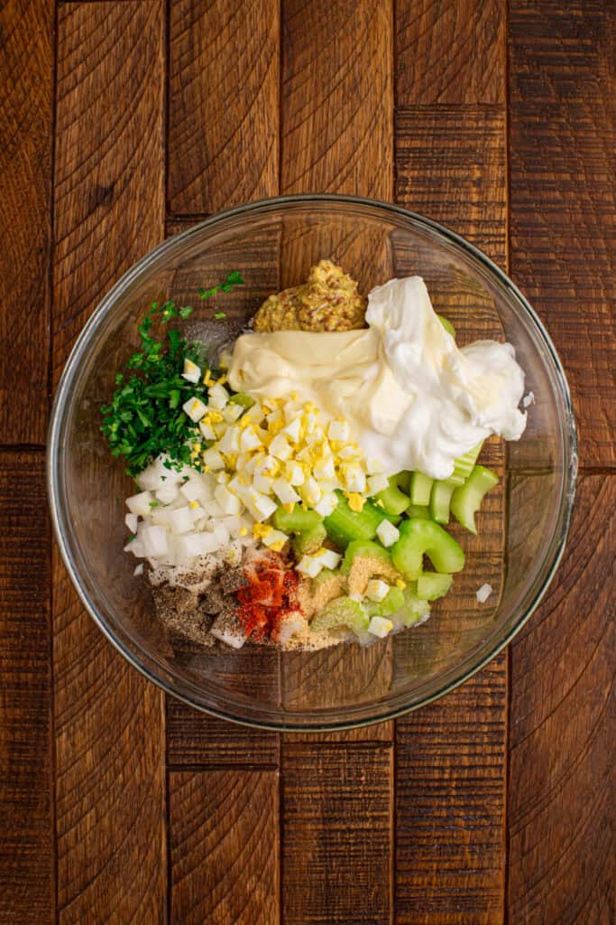 Creamy Sweet Potato Salad dressing ingredients with chopped eggs, celery, onion, parsley, mustard, and seasonings in a mixing bowl