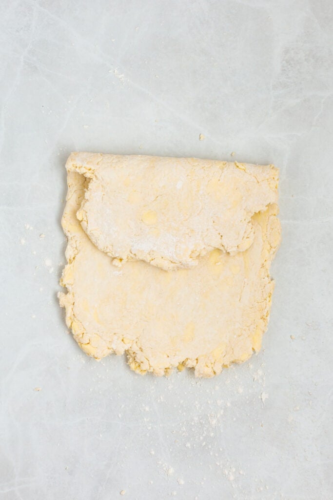 Sour cream biscuit dough folded over itself on a lightly floured work surface to create flaky layers.