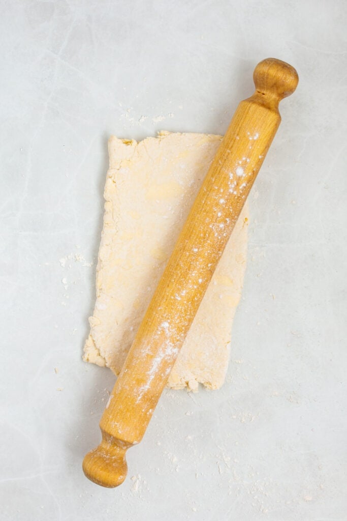 Wooden rolling pin over folded sour cream biscuit dough on a lightly floured surface.