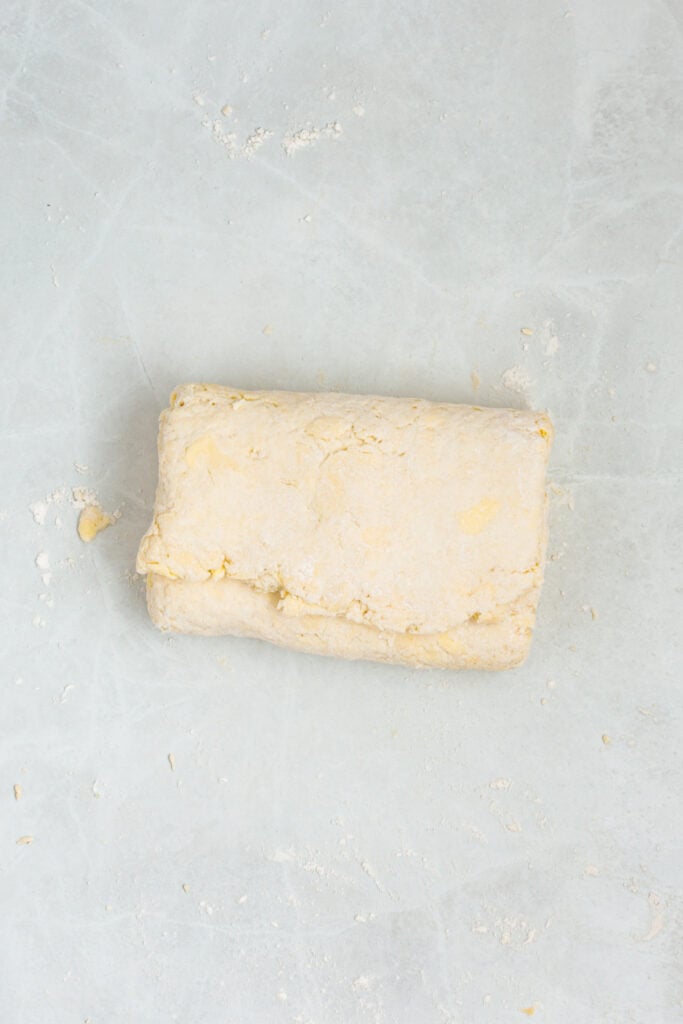 Folded sour cream biscuit dough resting on a lightly floured work surface.