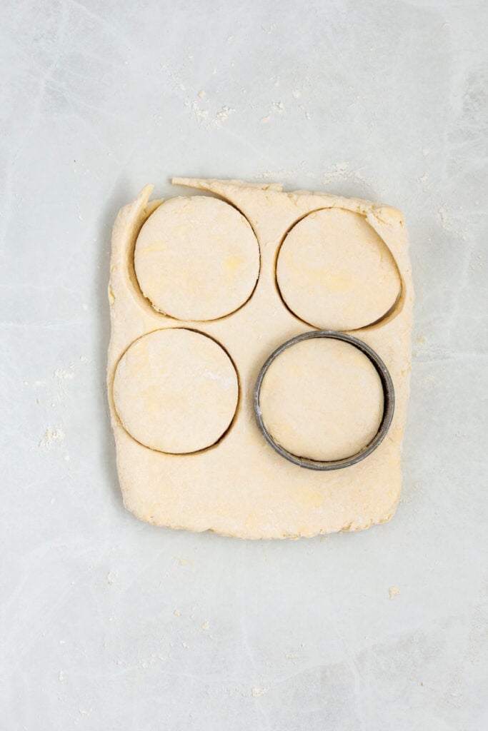 Round biscuits being cut from rolled sour cream biscuit dough with a metal biscuit cutter.