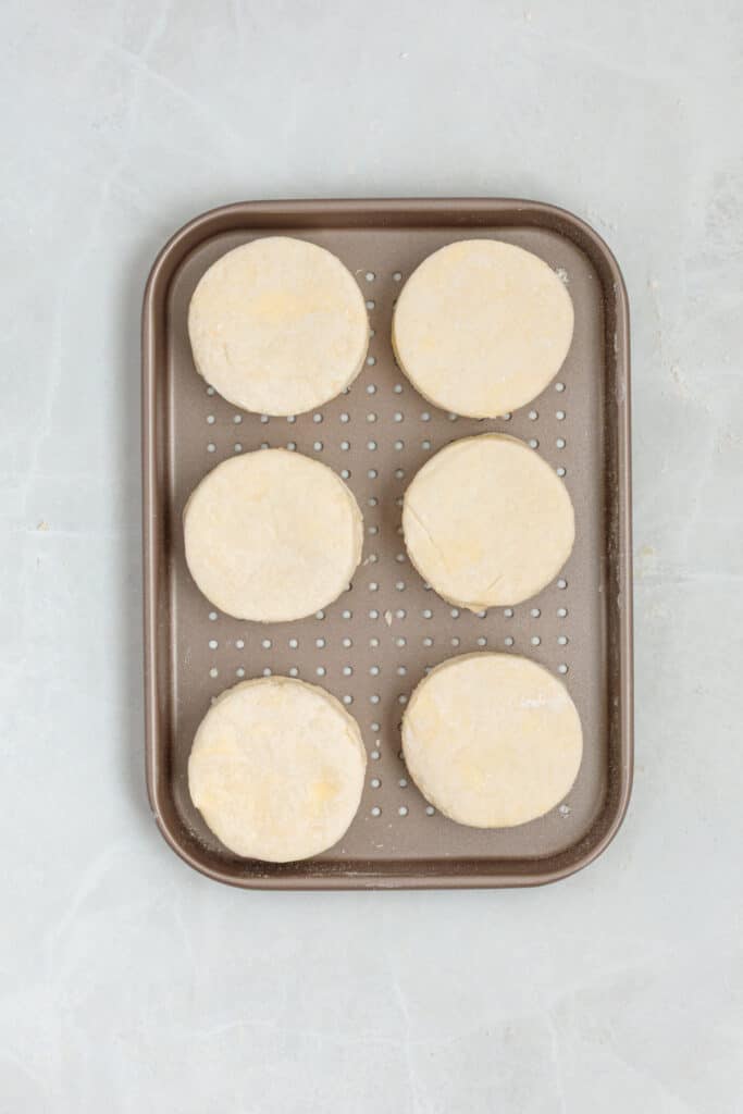 Six unbaked sour cream biscuits arranged on a perforated air fryer tray.
